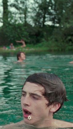 a man in the water with his tongue out and people swimming behind him, all looking at something off camera