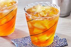 two glasses filled with drinks sitting on top of a wooden table next to a blue napkin