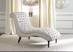 a white chaise lounge chair in front of a window with curtains and chandelier