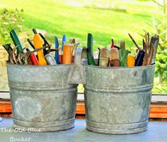 two buckets filled with pens and pencils sitting on a window sill in front of a grassy field