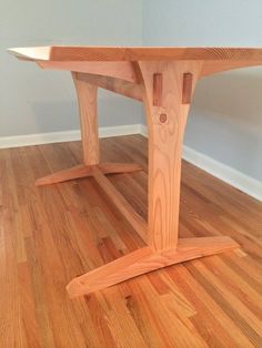 a wooden table sitting on top of a hard wood floor next to a white wall