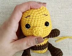 a hand holding a small yellow crocheted stuffed animal with black eyes and nose