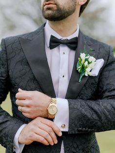 a man in a tuxedo with a watch on his lapel and flower boutonniere