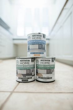 three cans of paint sitting on top of a tile floor