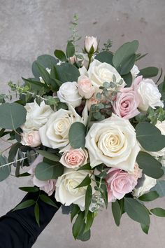 a bridal bouquet with white and pink roses, eucalyptus leaves and greenery is held by someone's hand