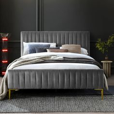 a bed with grey velvet upholstered headboard and foot board in front of a black wall