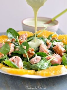 a salad with spinach and salmon being drizzled with dressing from a spoon