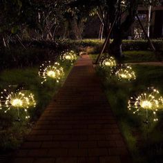 some lights that are on the side of a path in the grass near trees and bushes