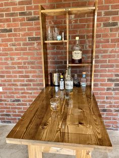 a wooden table with liquor bottles and glasses on it in front of a brick wall