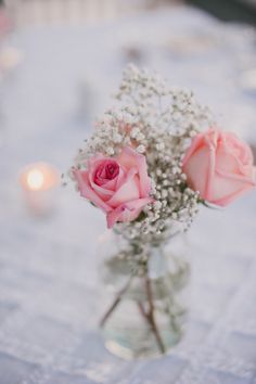 two pink roses in a glass vase on a table with baby's breath flowers