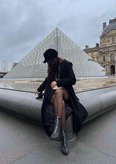 a woman sitting on top of a roof next to a glass pyramid in the background