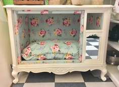 a white cabinet with flowers on it and a pillow in the bottom drawer that is open