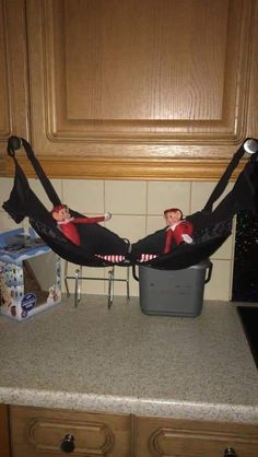 two men in red shirts and black pants are sitting in a hammock on the kitchen counter