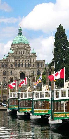 three paddle boats are docked in front of a large building with flags on it's sides