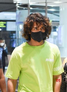 a man wearing a black face mask and green t - shirt at an airport terminal