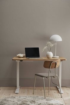 a laptop computer sitting on top of a wooden desk next to a white vase and lamp