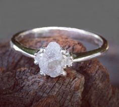 a white diamond ring sitting on top of a piece of wood next to a rock