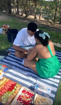 a man and woman sitting on top of a blue and white towel next to food