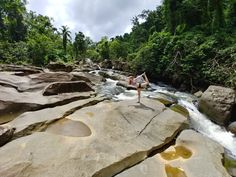 a woman doing yoga on rocks in the middle of a river surrounded by greenery