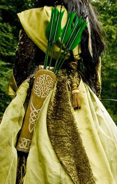 a woman dressed in medieval clothing with arrows sticking out of her hair and wearing a long yellow dress