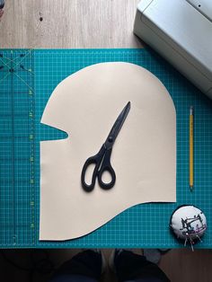 a pair of scissors sitting on top of a cutting mat next to a paper mask