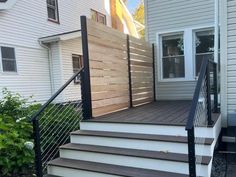 a wooden deck next to a white house with black handrails and stairs leading up to the front door