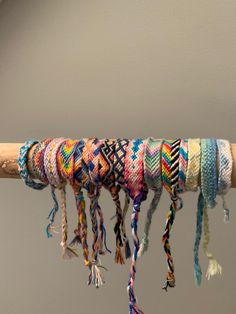 multicolored bracelets are hanging from a wooden stick with tassels on it