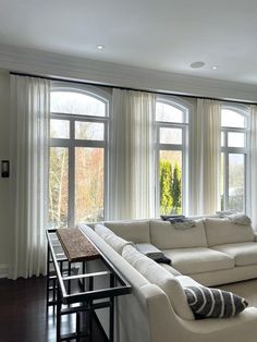 a living room filled with white furniture and large windows covered in sheered drapes