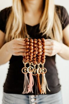 a woman holding several wooden beads with tassels on each bead and two key chains