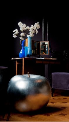 a large metal ball sitting on top of a wooden floor next to a blue vase with white flowers