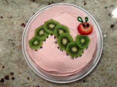 a pink cake decorated with kiwi slices and a strawberry on the top is sitting on a plate