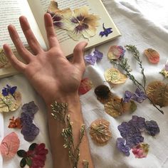 a person's hand on top of an open book surrounded by pressed flowers and leaves