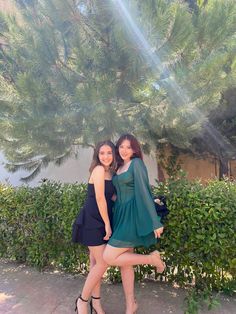 two women are posing for the camera in front of a tree