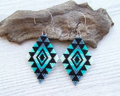 a pair of blue and black beaded earrings sitting on top of a piece of wood