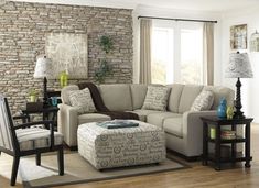 a living room filled with furniture and a stone wall behind the sectional couch is a footstool that sits on top of a rug