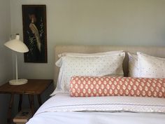 a bed with white and orange pillows on top of it next to a night stand