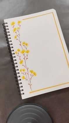 a spiral notebook with yellow flowers on it sitting next to a black plate and cup