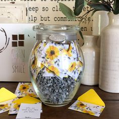 a jar filled with yellow and white flowers on top of a table next to cards