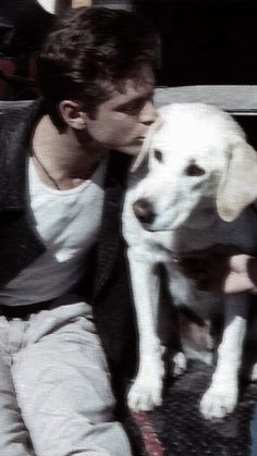 a man sitting on the ground kissing his dog