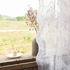 a vase sitting on a window sill next to a white lace curtain with flowers in it