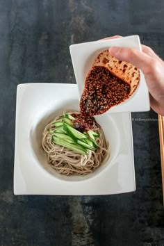 someone is dipping sauce on some noodles in a white bowl with chopsticks next to it