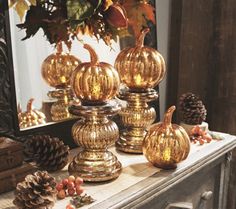 gold pumpkins and pine cones are sitting on a mantle in front of a mirror