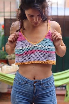 a woman wearing jeans and a crochet top is holding her hand on her hip