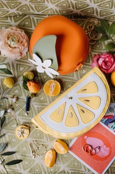 an assortment of fruit and flowers on a table with a yellow purse next to it