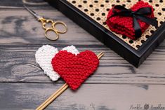 two crocheted hearts sitting on top of a table next to a pair of scissors