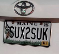 the license plate for this vehicle is being displayed in front of a white car with pine trees on it