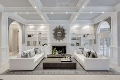 a living room filled with white furniture and a fire place in the middle of it