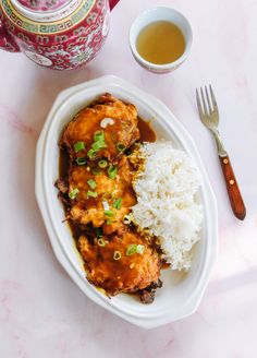 a white plate topped with meat covered in sauce and rice