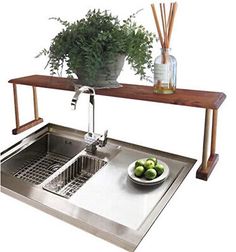 a stainless steel sink under a wooden shelf with a bowl of green apples on it