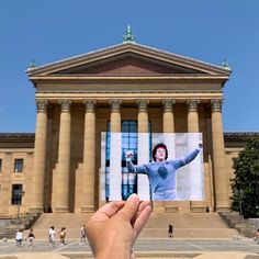 a person holding up a photo in front of a building with pillars and columns on it